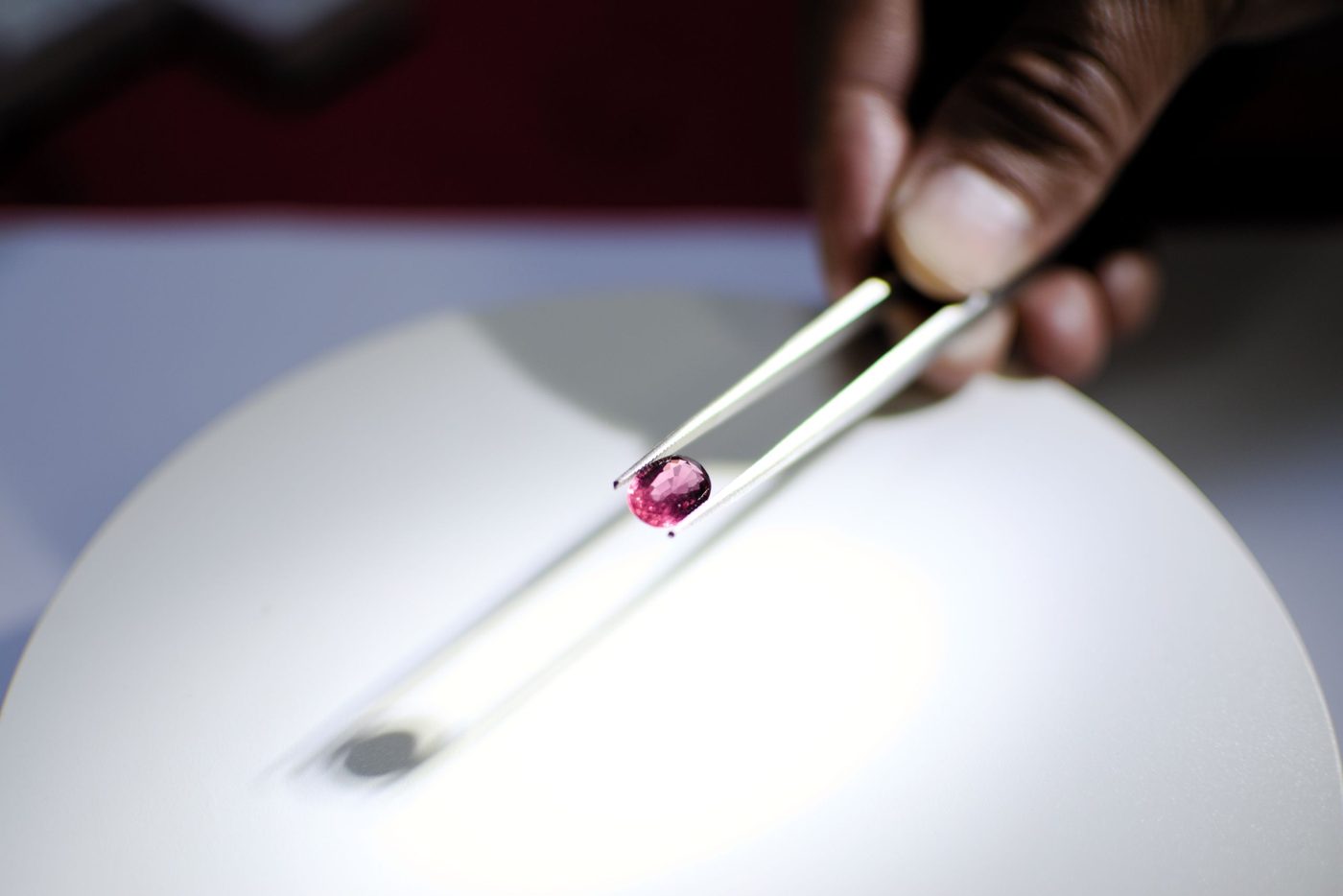 A gemstone held up in tweezers and examined against the light before it is bought.