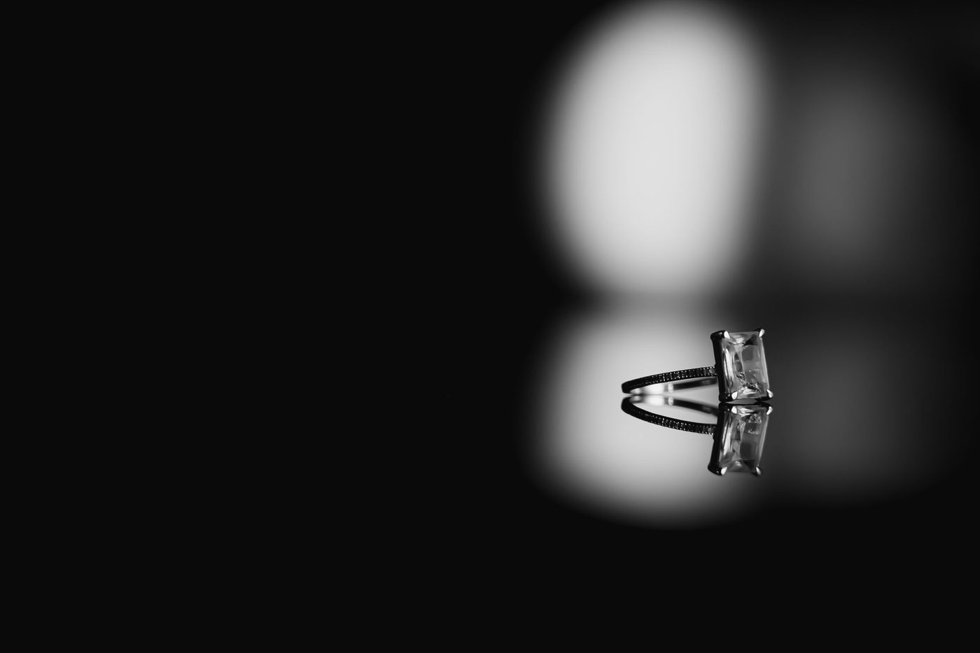 A diamond solitaire ring lit for close inspection on a dark reflective surface.