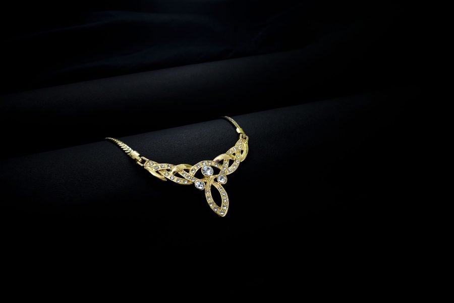 A gold necklace set with pavé diamonds, draped diagonally on a black ground.