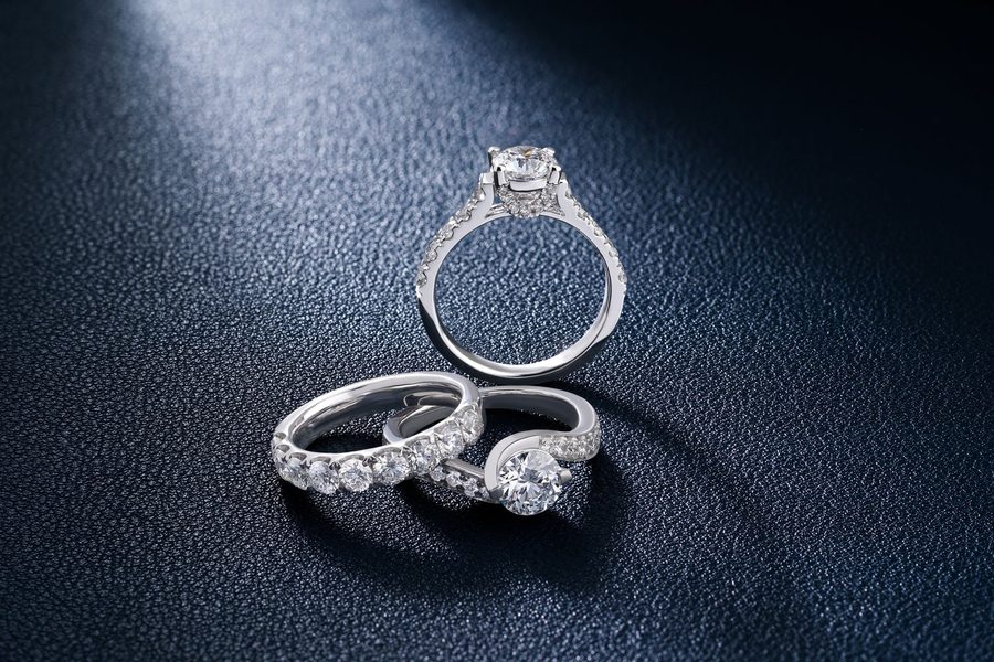 Three diamond rings — a plain band and two solitaires — laid out on dark leather under a single light.